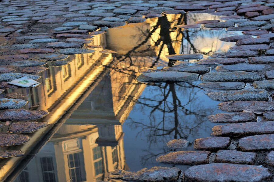 Reflection of an Old Montreal stone heritage building in a cobblestone puddle