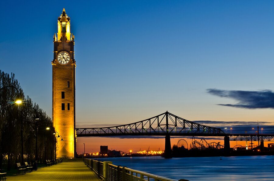 Montreal Clock Tower lit up at sunrise with the Jacques-Cartier Bridge in the distance