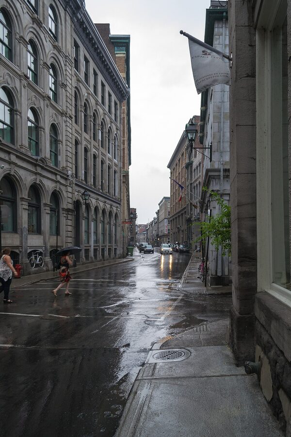 Rue Saint-Paul in Old Montreal on a rainy day, person with red umbrella walking past stone buildings